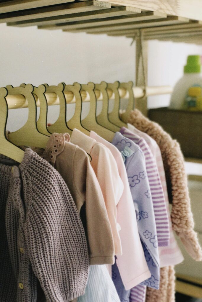 A collection of pastel baby clothes hanging neatly on wooden hangers in a stylish wardrobe.